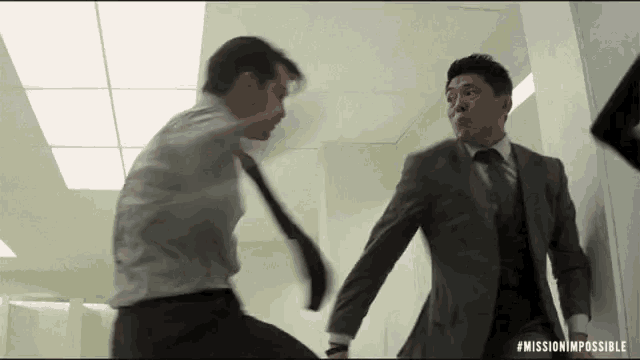 two men in suits and ties are fighting each other in a room .