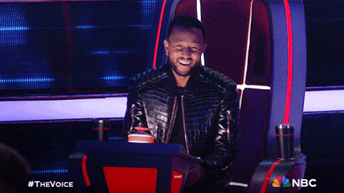 a man in a leather jacket is sitting in a chair with a nbc logo behind him
