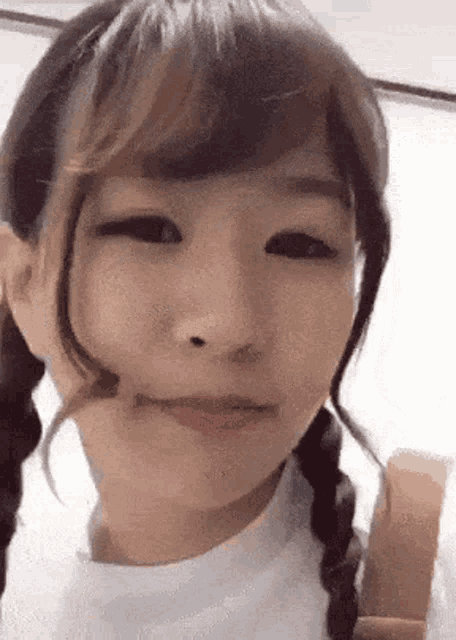a close up of a girl 's face with pigtails and a white shirt .