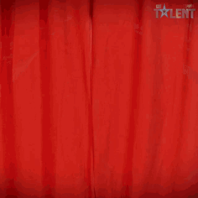 a man with a beard is standing in front of a red curtain with got talent written on it