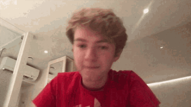 a young man in a red shirt is making a funny face while looking at the camera .