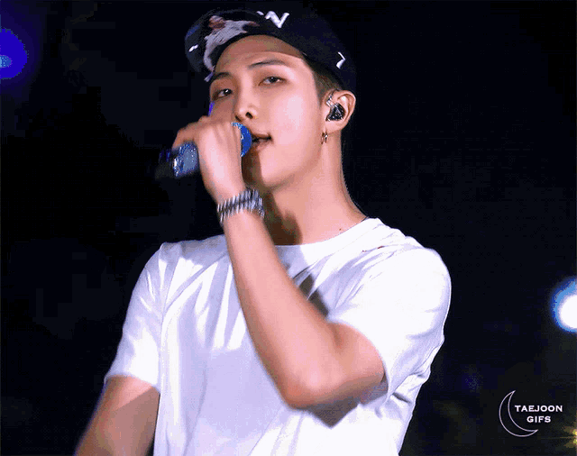 a man wearing a white shirt and a black hat is singing into a microphone with taejoon gifs in the corner