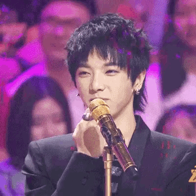 a young man is singing into a microphone in front of a crowd of people .