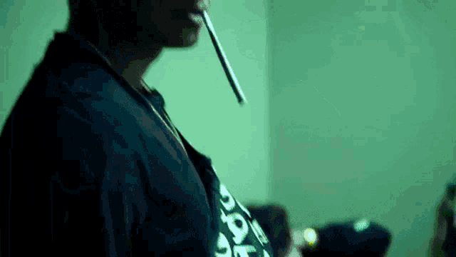 a man in a black shirt is smoking a cigarette in a room .