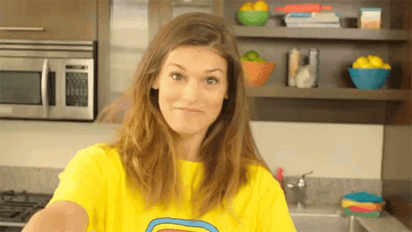 a woman wearing a yellow shirt with a rainbow on it stands in a kitchen