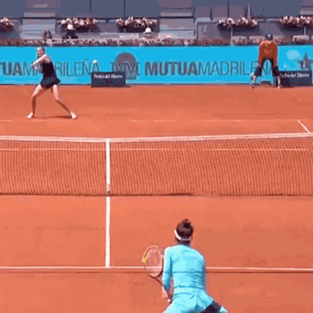 a woman is holding a tennis racquet on a tennis court in front of an advertisement for mutua madrid .