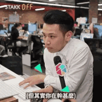 a man is sitting at a desk with a microphone in front of him and a sign that says stakk off