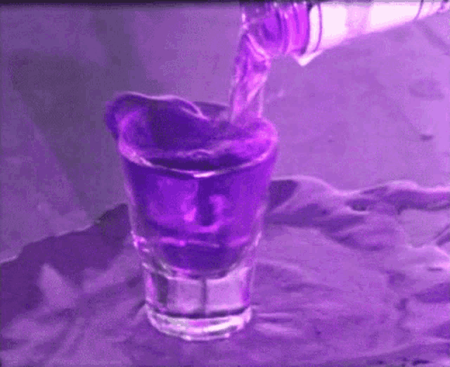 a purple liquid is being poured into a shot glass .
