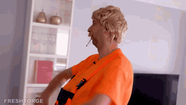 a man in an orange shirt is smoking a cigarette in front of a bookshelf that says freshtorge