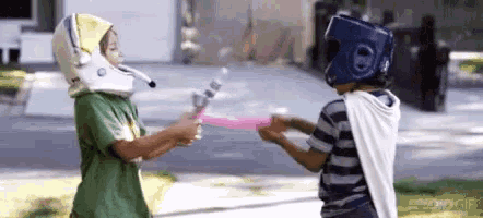 two young boys wearing helmets and capes are holding swords .
