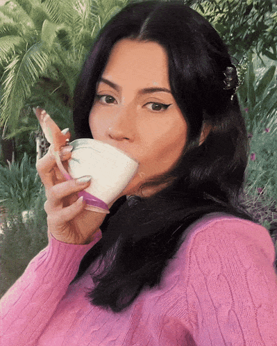 a woman in a pink sweater drinks from a cup