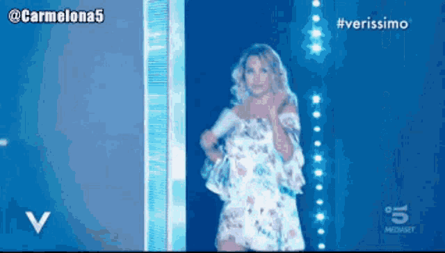 a woman in a floral dress stands in front of a blue background with the words verissimo on it