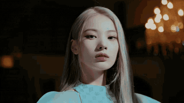a close up of a woman 's face with a light behind her and a chandelier in the background