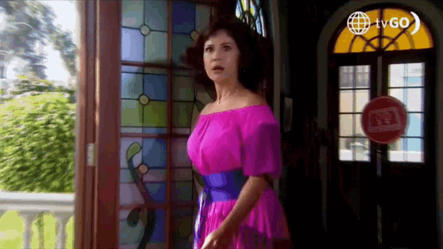 a woman in a pink off the shoulder dress stands in front of a stained glass window .
