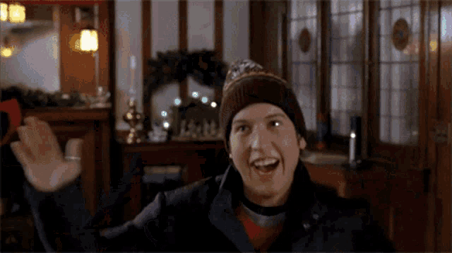 a man wearing a knitted hat and a leather jacket is waving his hand