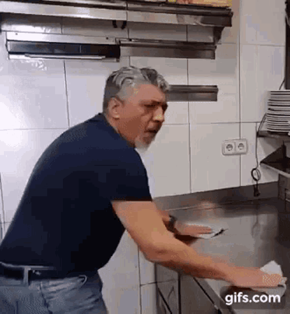 a man with a beard is cleaning a counter in a kitchen with a towel .