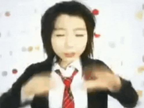 a girl wearing a suit and tie is making a heart shape with her hands .