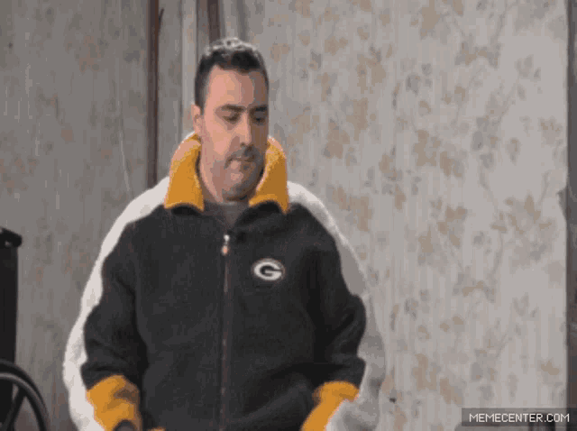 a man wearing a green bay packers jacket stands in front of a wall