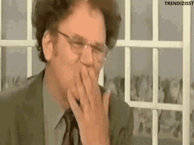 a man in a suit and tie is covering his mouth with his hand while laughing .