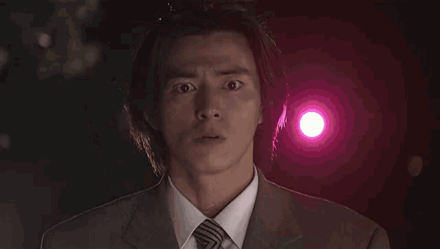 a man in a suit and tie is looking at the camera with a pink light in the background .