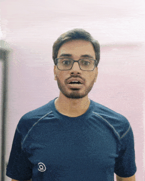 a man wearing glasses and a blue shirt with the letter q on the front makes a surprised face
