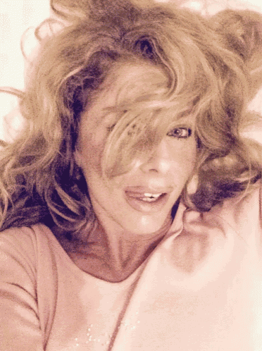 a woman with her hair blowing in the wind is wearing a pink shirt