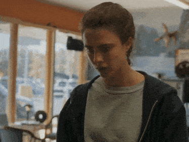 a woman wearing a grey shirt and a black hoodie stands in a room