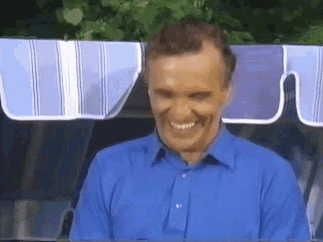 a man in a blue shirt is smiling while sitting under a blue and white striped awning .