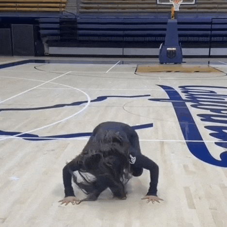 a woman is doing a handstand on a basketball court with a basketball hoop in the background