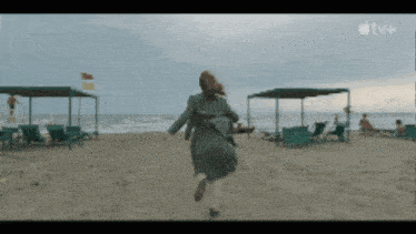 a woman in a green coat is running on a beach with an apple tv logo in the background