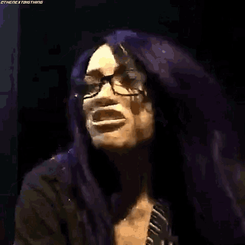 a woman with purple hair and glasses is making a funny face in a dark room .