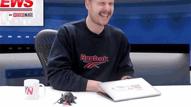 a man wearing a reebok sweatshirt is sitting at a desk