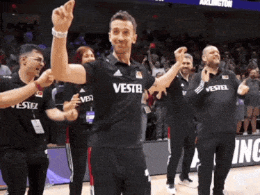 a man wearing a black vestel shirt stands in front of a crowd