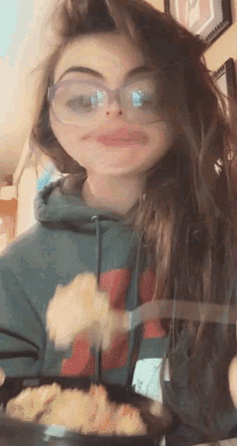 a girl wearing glasses and a hoodie with the letter m on it is eating food