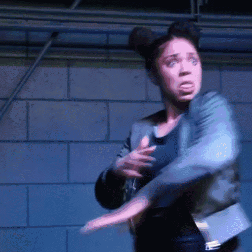 a woman in a leather jacket is dancing in front of a blue brick wall