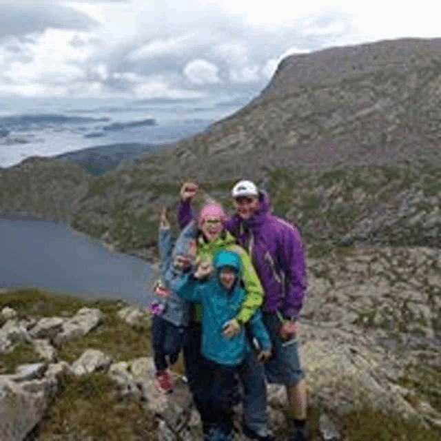 a family is posing for a picture on top of a mountain with a lake in the background .