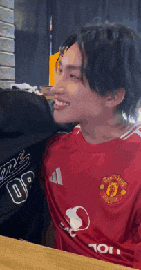 a man wearing a red manchester united jersey smiles