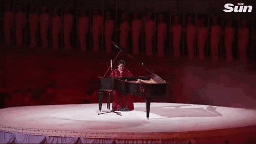 a woman in a red dress is playing a piano on a stage with the sun written on the bottom right