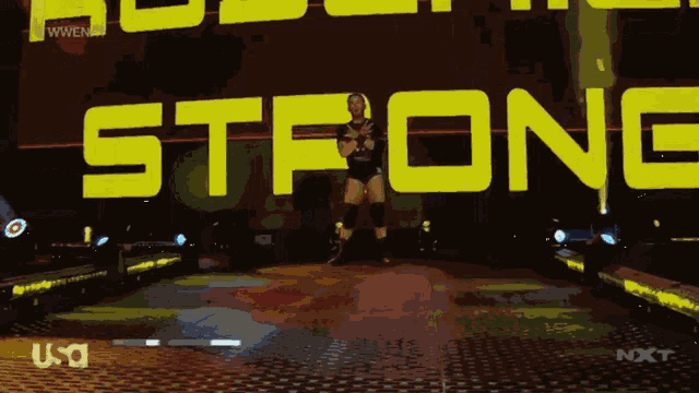a wrestler stands in front of a sign that says " strong "