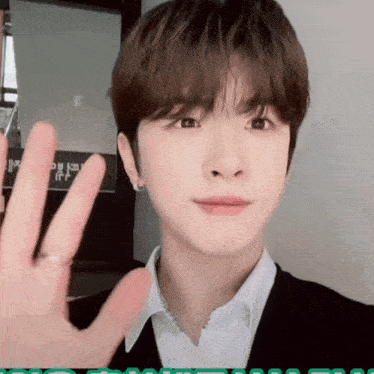 a young man wearing a white shirt and a black jacket waves his hand