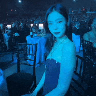 a woman in a blue dress sits in a chair in front of a crowd of people