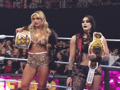 two women are standing in a wrestling ring holding their championship belts