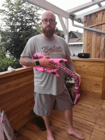 a man wearing a shirt that says boston holds a pink guitar