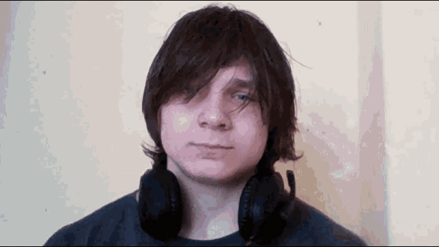 a young man with long hair wearing headphones around his neck