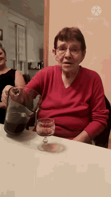 a woman in a red sweater sits at a table with a pitcher and a glass