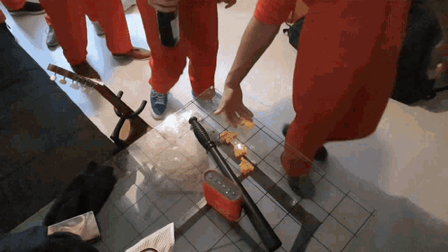 a group of people in orange jumpsuits are standing around a table with a speaker and a bat