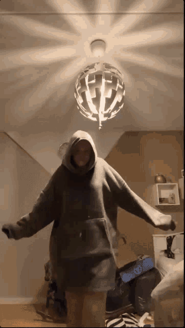 a person in a grey hoodie is standing in front of a chandelier