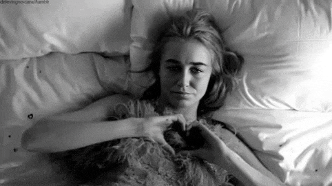 a black and white photo of a woman laying on a bed making a heart with her hands .