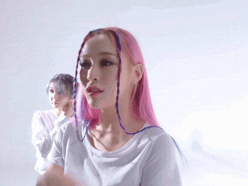 a woman with pink and purple hair is wearing a white top