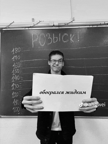 a young man holds up a piece of paper with russian writing